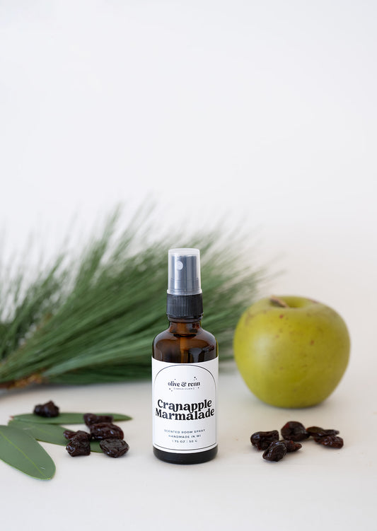 Bottle room spray of 'Cranapple Marmalade' with an apple and raisins on a white background